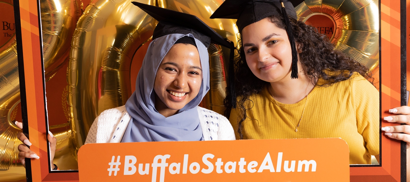 Two students posing with an alumni sign